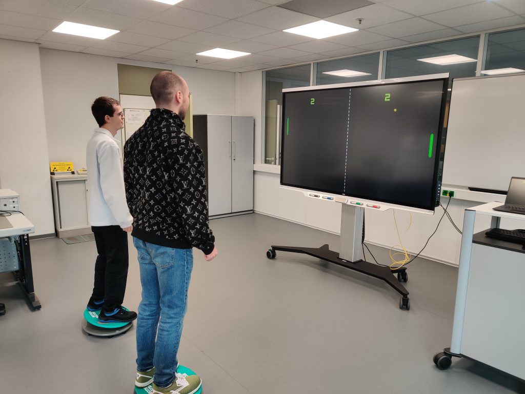 Die "Motion Masters" von Max und Yannic, die die Ausbildung zum Elektroniker für Informations- und Systemtechnik absolvieren, in Aktion: Zwei Männer stehen jeweils auf einem Motion Board und spielen gegeneinander ein Videospiel. Vor ihnen steht der große Bildschirm.