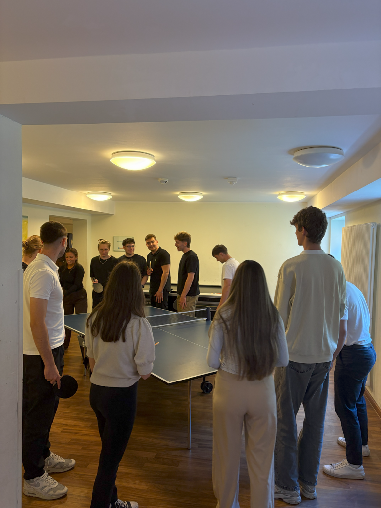 Eine Gruppe von Personen spielt Tischtennis in einem Aufenthaltsraum.