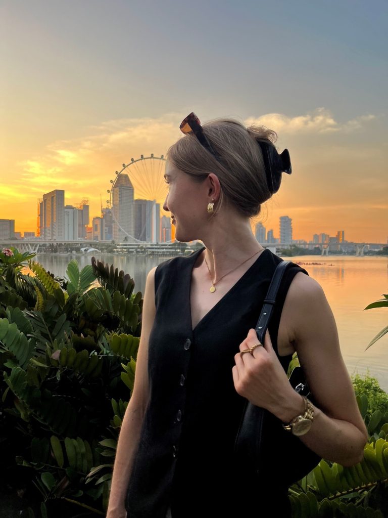 Janine dreht sich von der Kamera weg. Im Hintergrund sieht man die Skyline von Singapur. Die Sonne geht gerade unter.