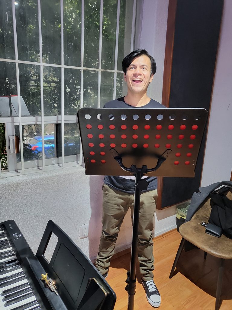 Daniel steht in einem kleinen Raum vor einem Notenständer und singt. Links vor ihm ist ein Keyboard zu sehen.