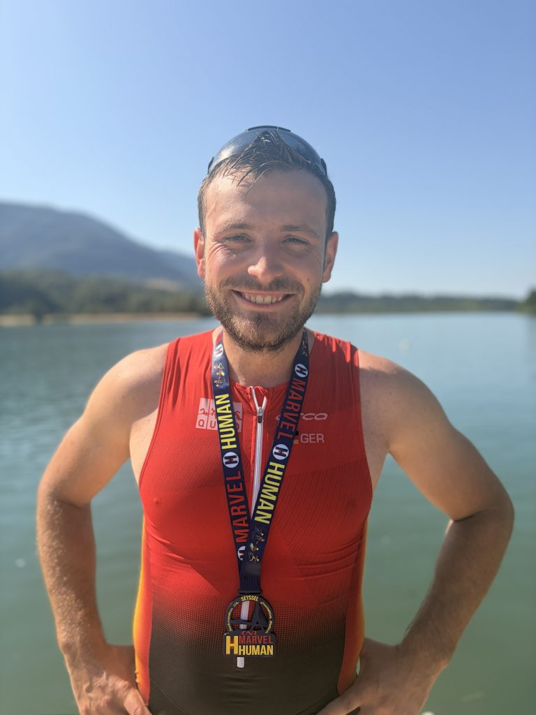 Profilbild von Marco im Trainingsoutfit. Hinter ihm ist unscharf ein See zu sehen.